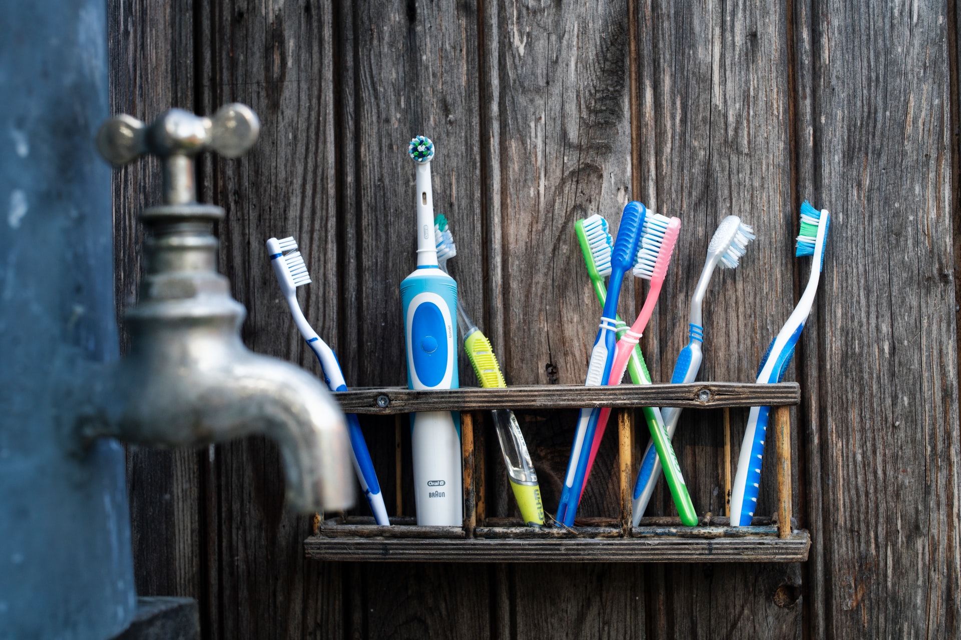 A wooden shelf of toothbrushes in assorted colors by a faucet