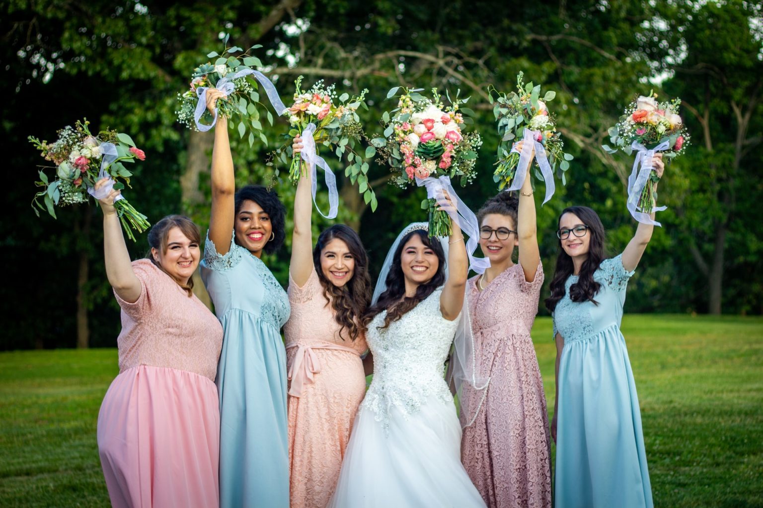 A bride and her bridesmaids smiling and holding their bouquets in the air