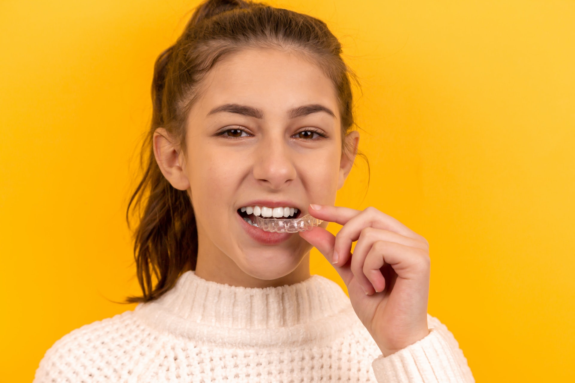 A girl putting in a clear retainer for dental alignment