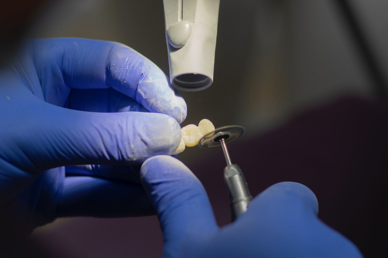 A person wearing purple latex gloves and polishing a dental bridge