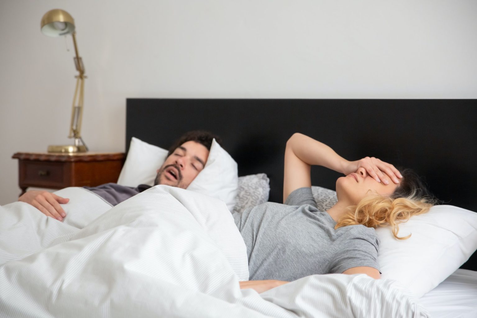 man snoring in bed with frustrated woman