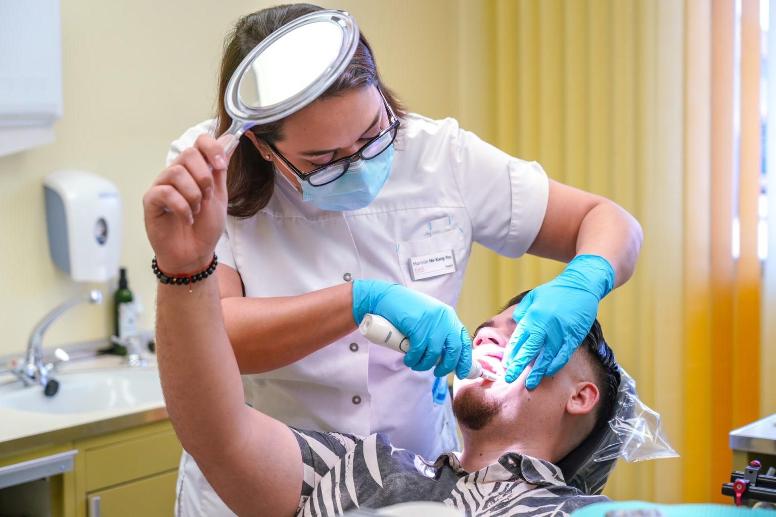 patient holding a mirror while receiving dental cleaning
