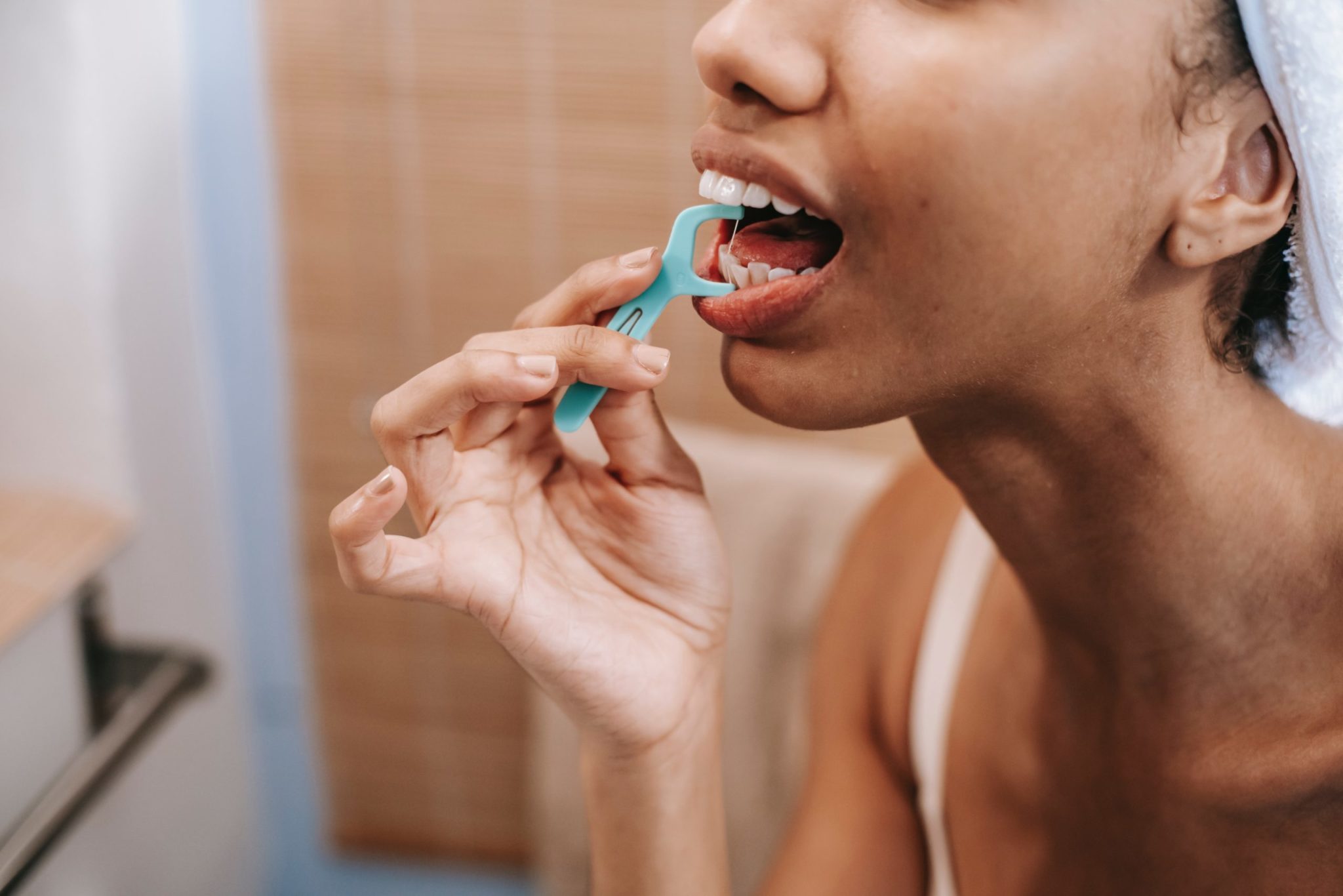 A woman cleans her teeth with a floss pick.