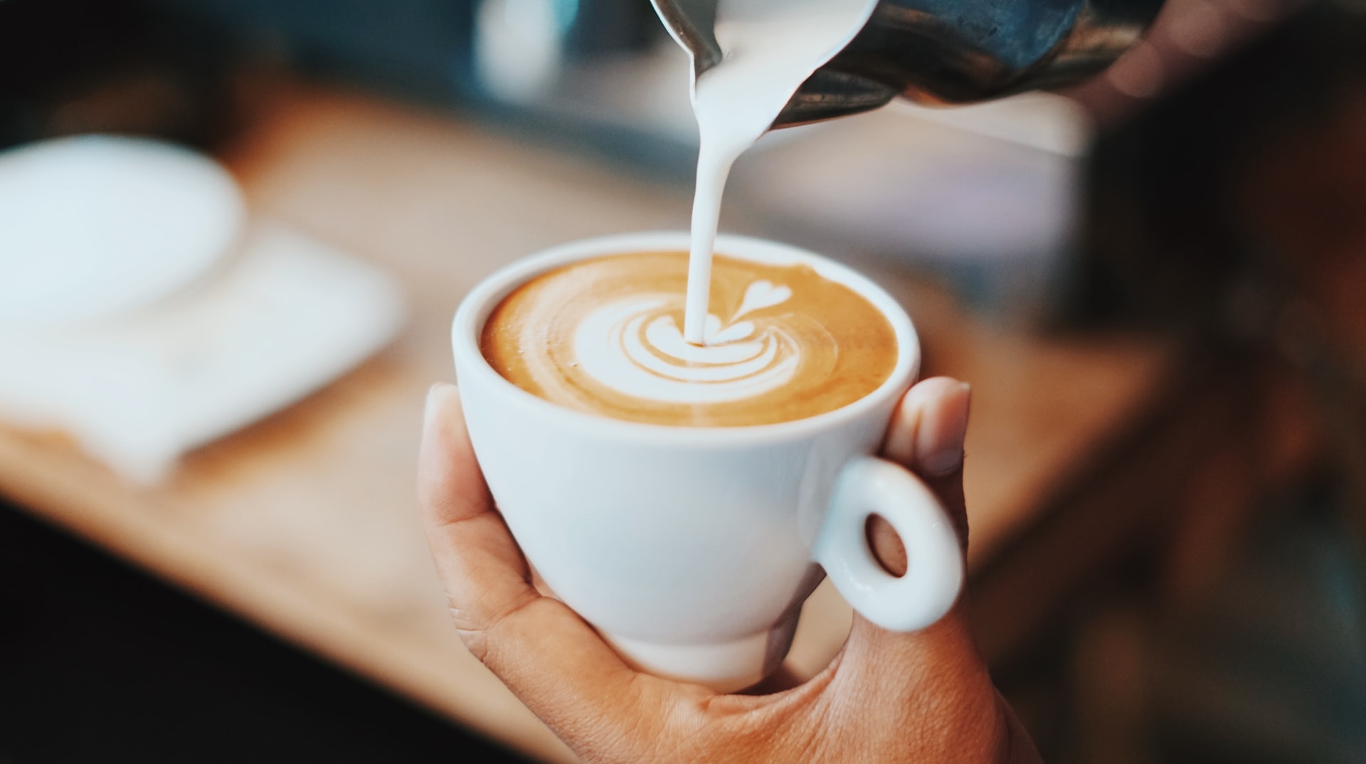 A barista pours cream into a coffee cup