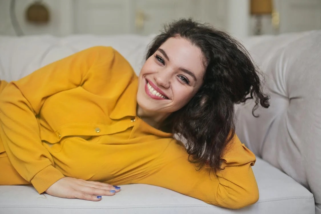 A woman lying on a sofa smiling with whitened teeth