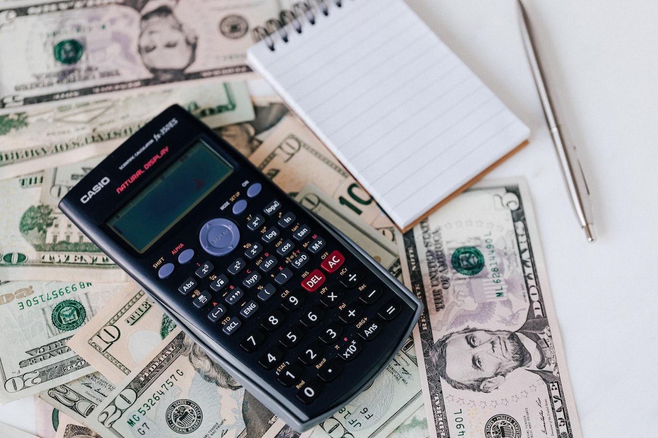 A calculator and a notepad placed on dollar bills