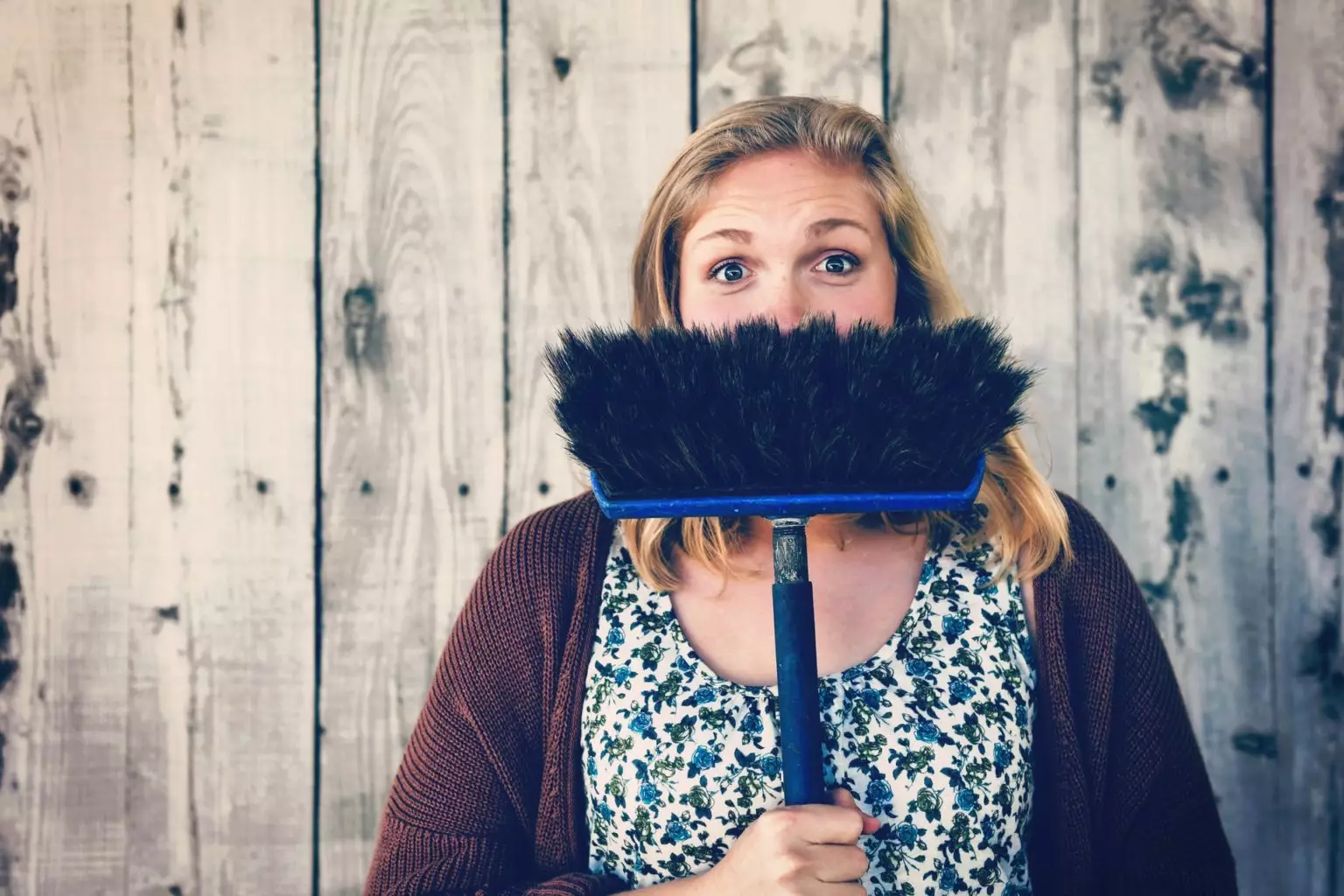 Woman holding broom upside down and hiding her teeth