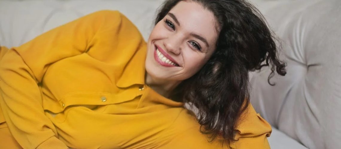 A woman lying on a sofa smiling with whitened teeth