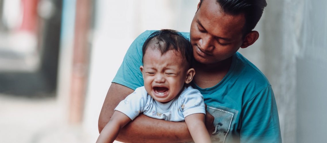 A man holding a crying child with tooth pain