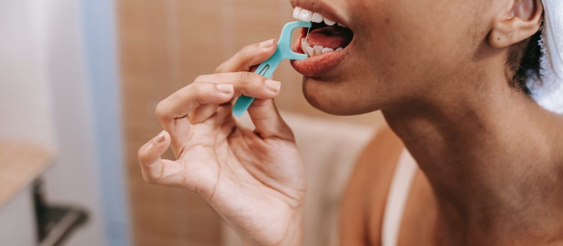 A woman cleans her teeth with a floss pick.