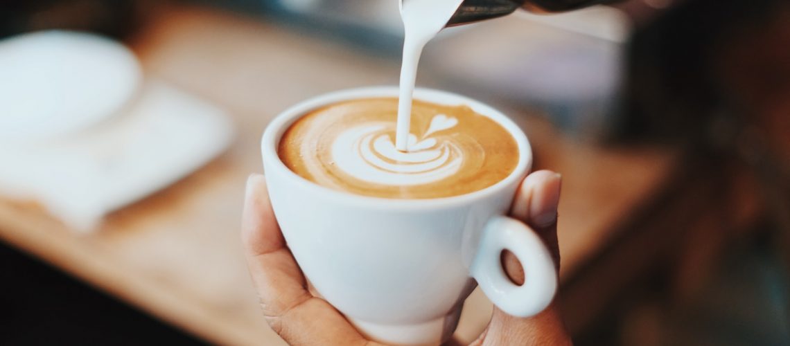 A barista pours cream into a coffee cup