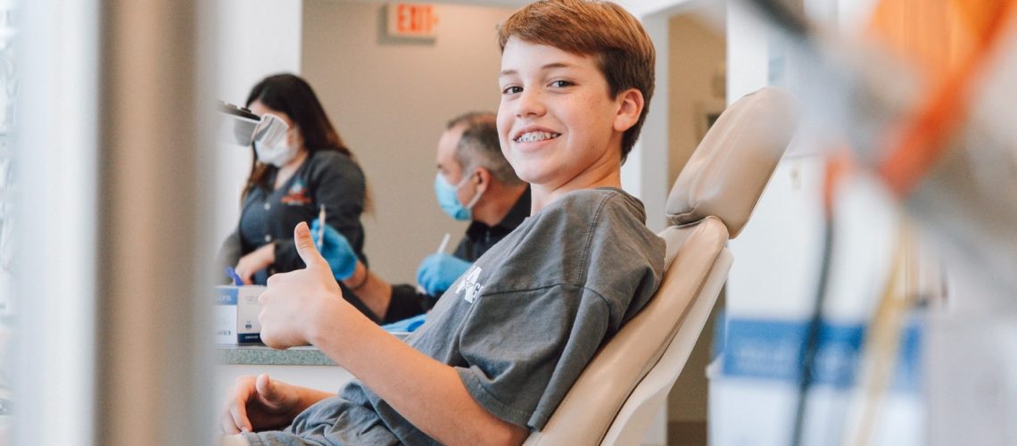 young boy smiling and giving a thumbs up in dental office